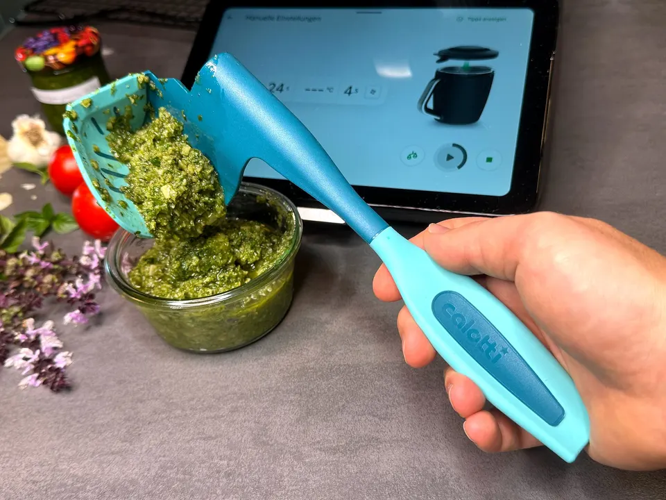 Pesto gleitet vom Calotti® Drehkellenspatel SILIKON+ in eine Glasschale, dahinter das Thermomix® TM7 Display